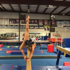 a person on a balance beam doing a handstand in an indoor gymnastics gym