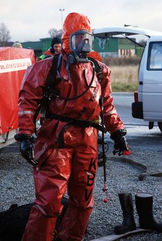 a man in red coveralls standing next to a fire hydrant wearing a gas mask