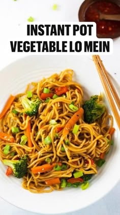 a white bowl filled with noodles and veggies next to chopsticks on a table