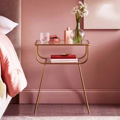 a pink bedroom with a gold side table and flowers on the nightstand next to it