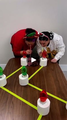 two people standing over a wooden table with bottles on it and yellow tape around them