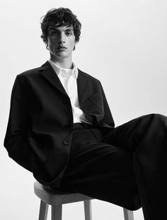 a young man sitting on top of a stool wearing a black suit and white shirt