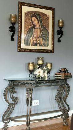 a painting on the wall above a console table with candles and flowers in front of it