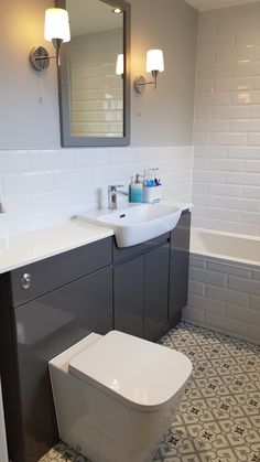 a white toilet sitting next to a sink in a bathroom under two mirrors on the wall