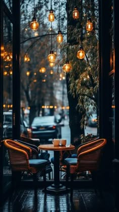 two wicker chairs sitting at a table in front of a window with lights hanging from it