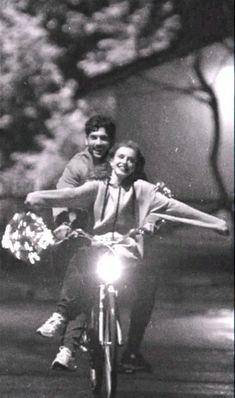 a man and woman riding on the back of a bike