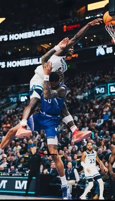 two basketball players jumping up to dunk the ball in front of an audience at a sporting event