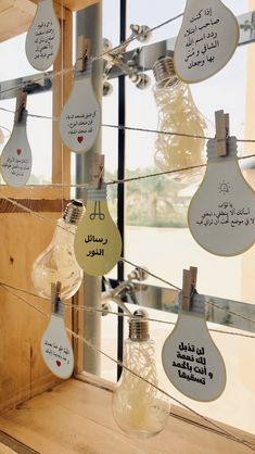 several light bulbs with arabic writing on them hanging from clothes pins in front of a window