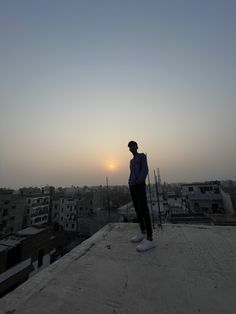 a man standing on top of a roof with the sun setting in the distance behind him