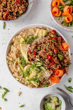 two bowls filled with rice and vegetables on top of a white table next to other dishes