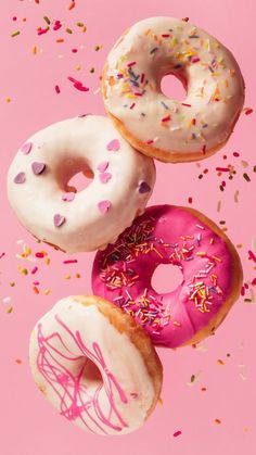 three donuts with pink frosting and sprinkles on a pink background