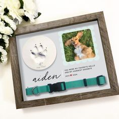 a dog's paw and handprints are displayed in a wooden frame next to flowers