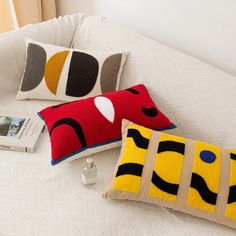 two decorative pillows on a bed next to a book and cell phone with an alarm clock in the background