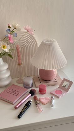 a white table topped with pink items and a lamp next to a vase filled with flowers