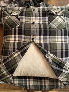 a green and white checkered shirt sitting on top of a wooden floor next to a pillow