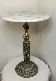 a table with a white marble top and gold metal base sitting on a round pillow