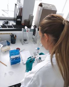 a woman in white lab coat sitting at a desk with microscope and test tubes on it