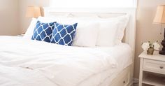 a white bed with blue and white pillows on top of it next to two nightstands