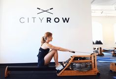 a woman sitting on top of a rowing machine in front of a city row sign