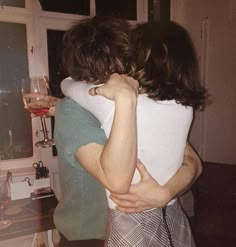 two people hugging each other in front of a kitchen counter with wine glasses on it