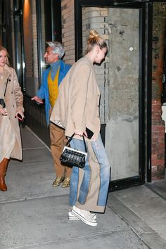 two people are walking down the sidewalk with one carrying a handbag and another holding a purse