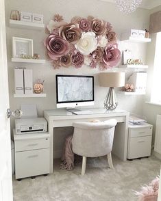 a white desk topped with a computer monitor next to a wall covered in paper flowers