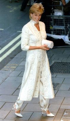 the woman is walking down the street in her white outfit and heels, she is smiling at the camera