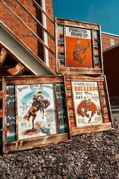 three framed posters on the side of a brick building next to a stair case and railing