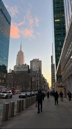 people are walking on the sidewalk in front of tall buildings and skyscrapers at sunset