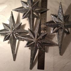 three silver glittered star ornaments on a white background next to a measuring tape and ruler