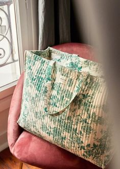 a green and white bag sitting on top of a pink chair next to a window