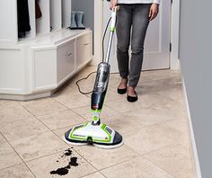 a woman is cleaning the floor with a green and white vacuum