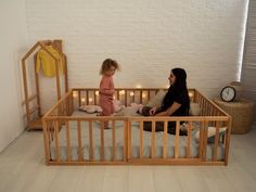 a woman and child sitting in a wooden crib with candles on the floor next to them