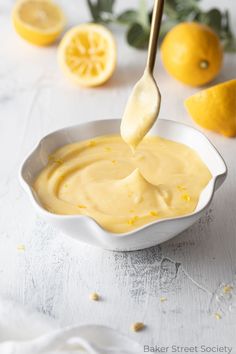 a white bowl filled with yellow sauce next to lemons