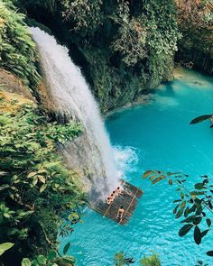 people are swimming in the blue water near a waterfall