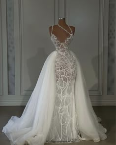 a white wedding dress on display in front of a wall with glass panels and beading