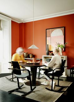 two people sitting at a table with chairs in front of them and an orange wall behind them