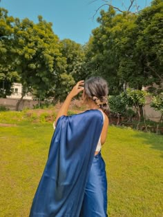 a woman in a blue cape standing on top of a lush green field