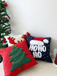 three christmas pillows sitting on top of a couch next to a christmas tree and other decorations