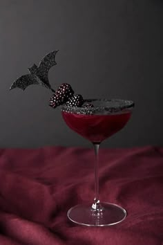 a halloween drink garnished with blackberries and sprinkles on a red cloth