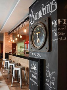 a clock mounted to the side of a wall next to stools in a restaurant