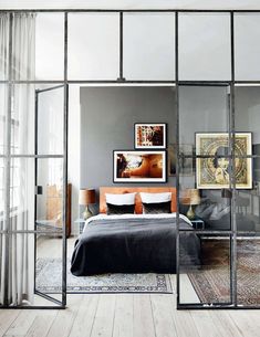 a bedroom with glass walls and a bed in the middle, surrounded by wooden floors