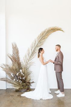 a bride and groom standing in front of a palm tree with their hands clasped together