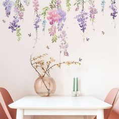 a white table topped with a vase filled with purple flowers next to a wall mural