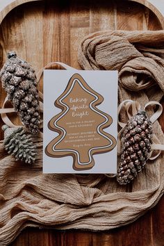 a card with a christmas tree on it and pine cones next to it, sitting on a wooden platter