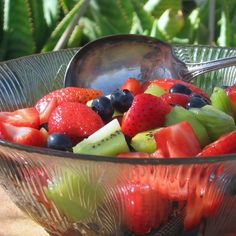 a glass bowl filled with lots of fruit and a metal spoon in the bowl next to it