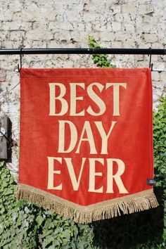 a red banner with the words best day ever hanging on a clothes line in front of a brick wall