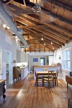 an open kitchen and dining room with wood flooring, exposed ceiling beams and white walls