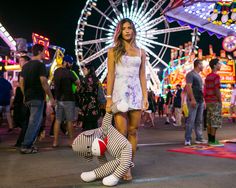 a woman standing next to a stuffed animal in front of a ferris wheel at night