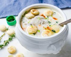 a white bowl filled with soup and dumplings next to crackers on a table